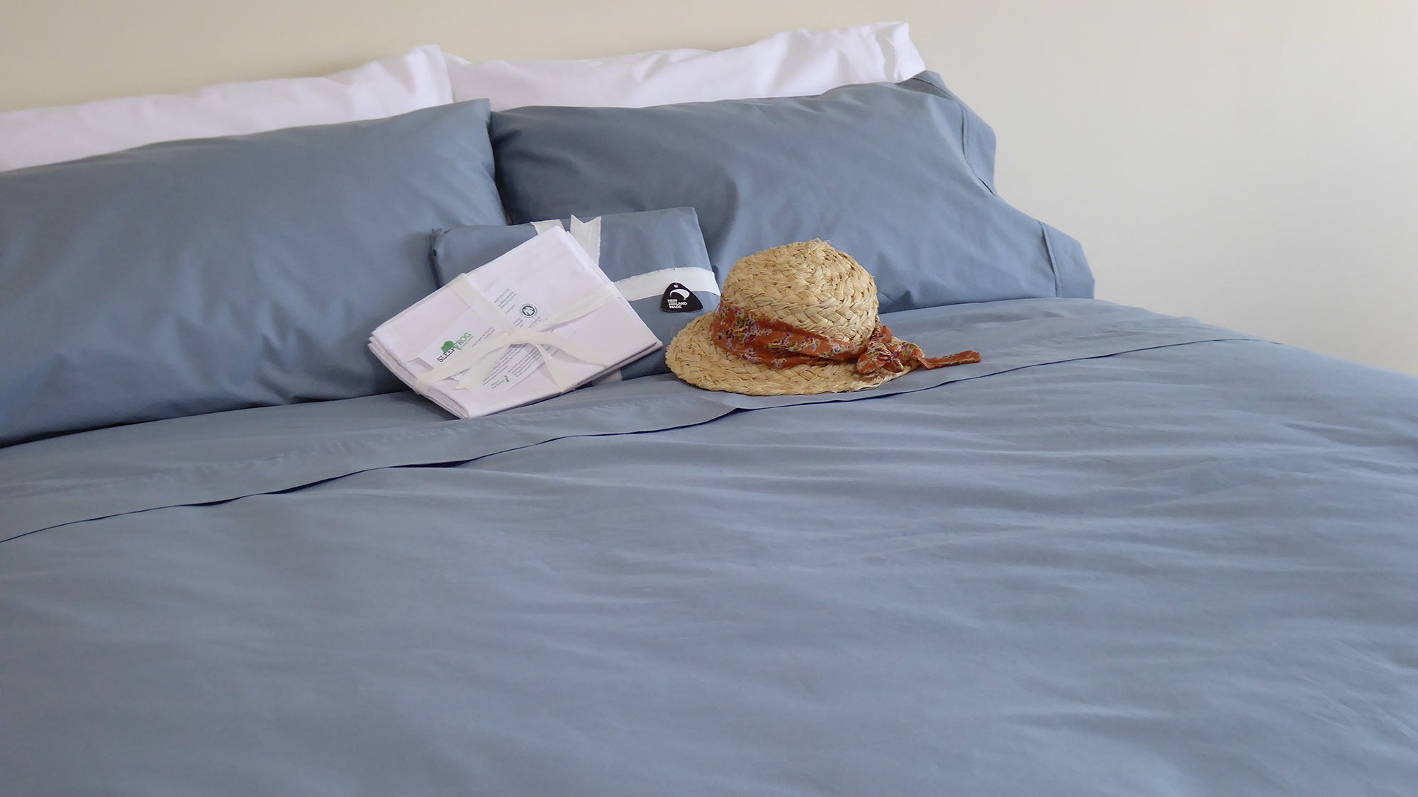 SleepFROG-Blue-and-White-Bed-Linen-on-bed-with-folded-sheets-and-sunhat